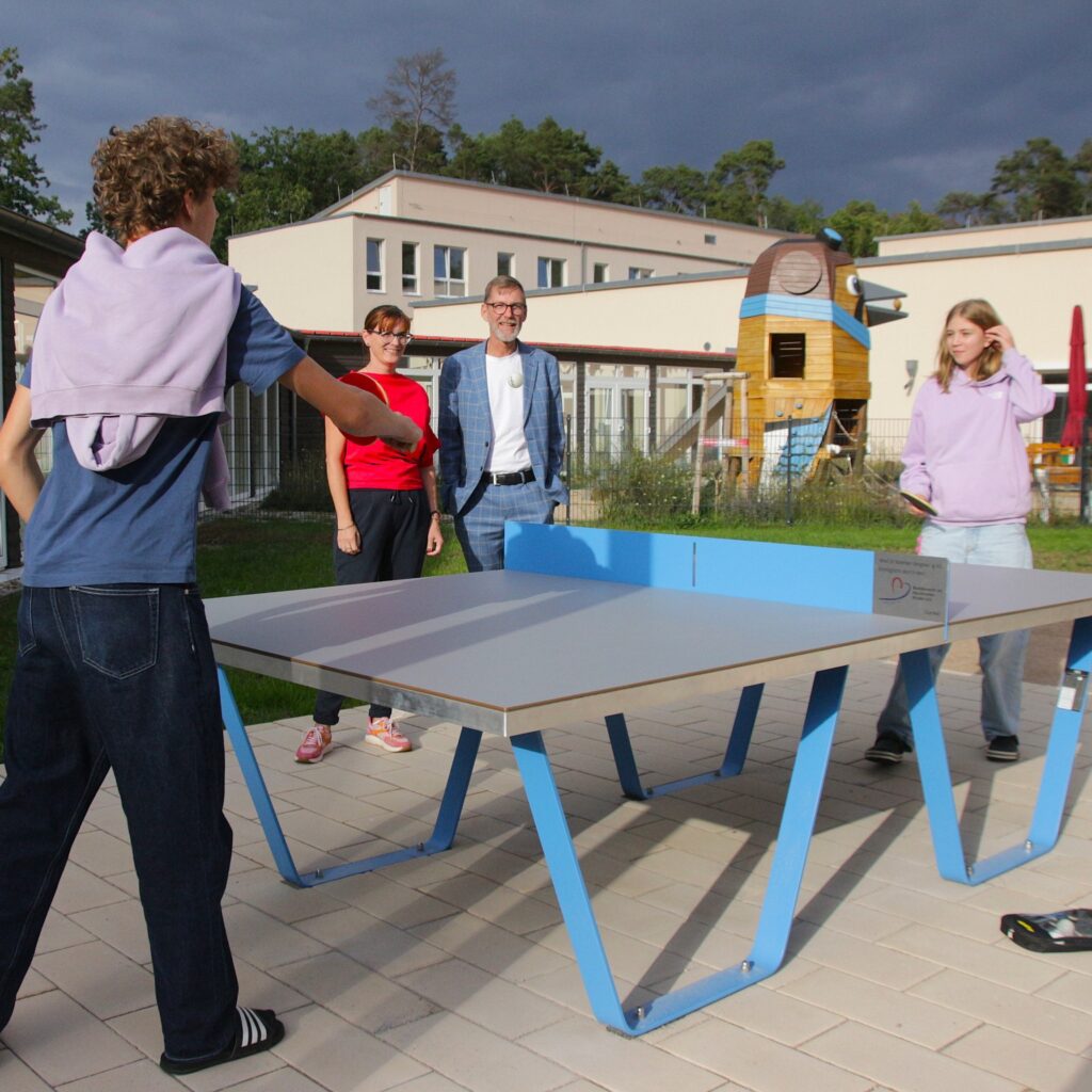 Sandra Hollmann (Vorstand BVHK) und Sebastian Kahnt (Geschäftsführer BVHK) gucken zwei Jugendlichen beim Tischtennisspielen auf dem Gelände der Nachsorgeklinik zu