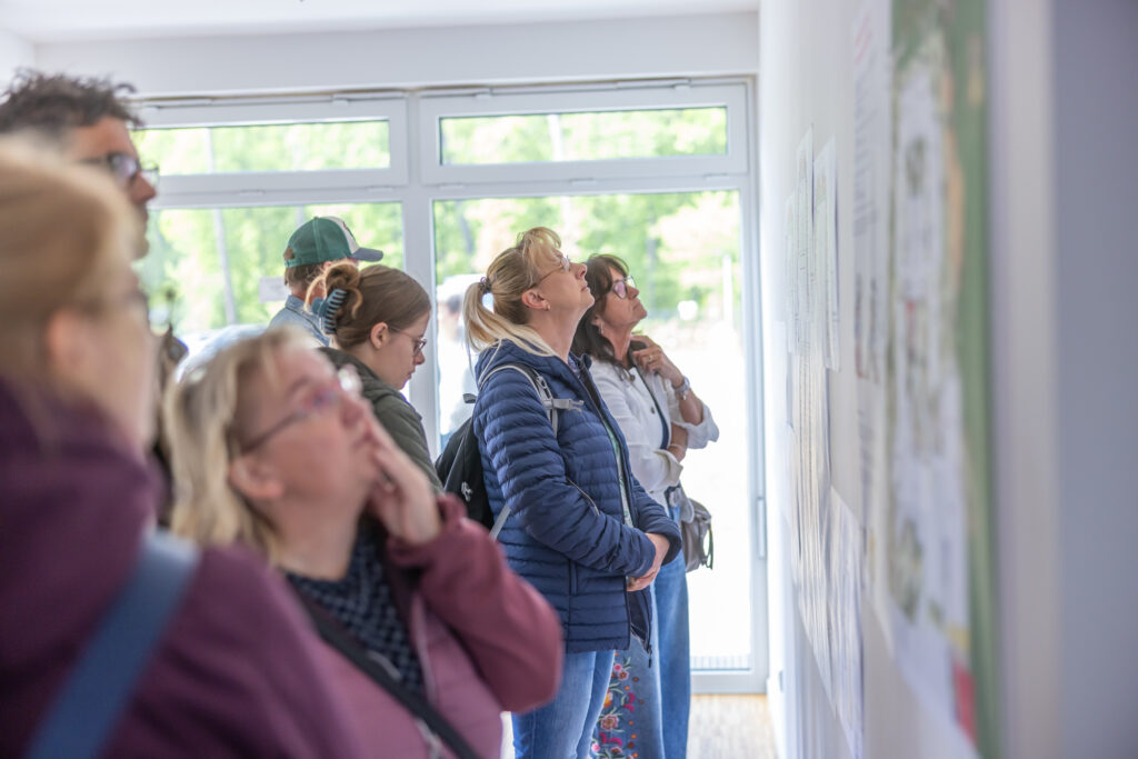 Besucher:innen betrachten Pläne dessen, was in und außerhalb der Nachsorgeklinik am Straussee geplant ist